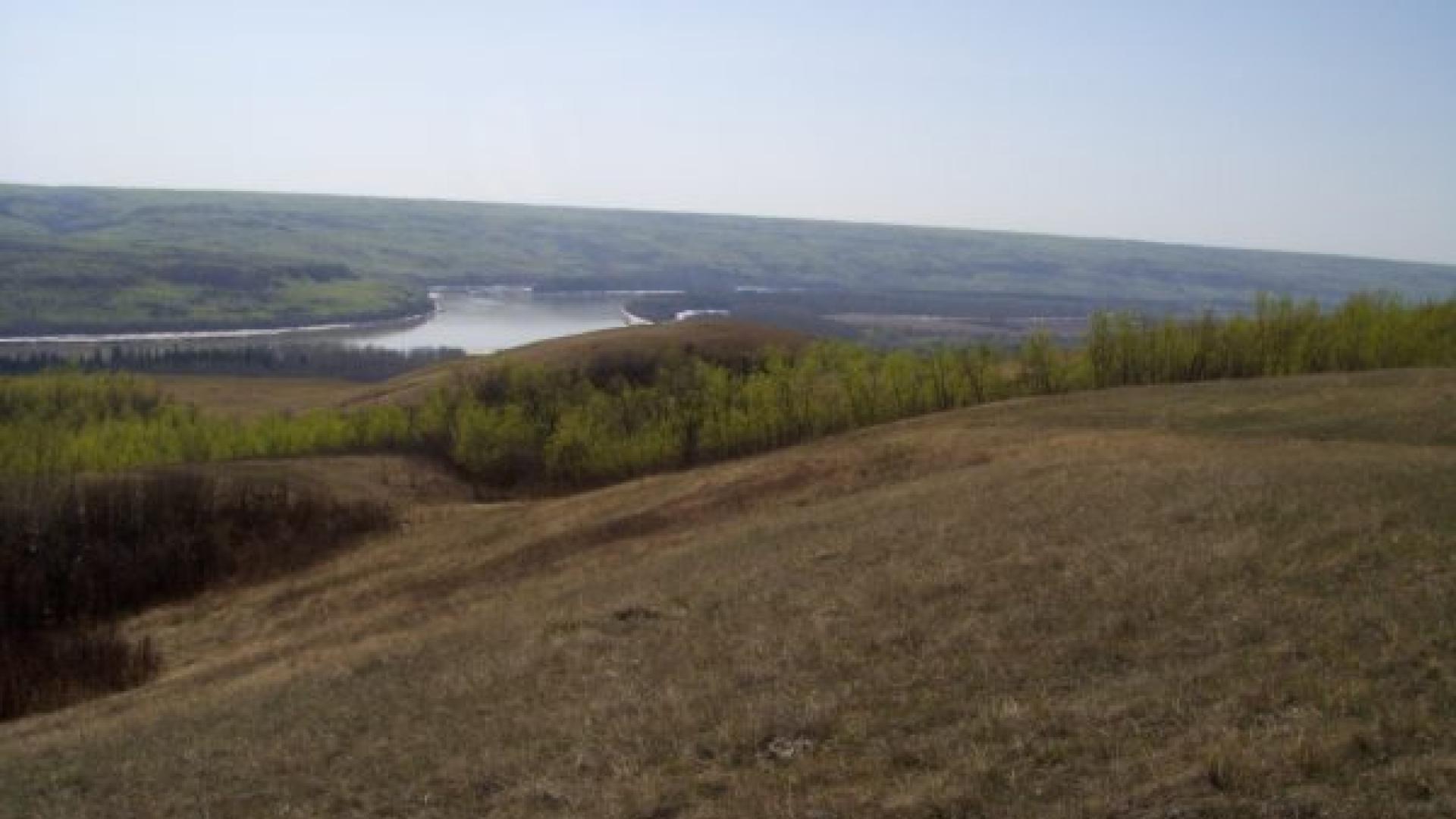 Landscape of a valley that is divided by a river. The sun is setting on the horizon.